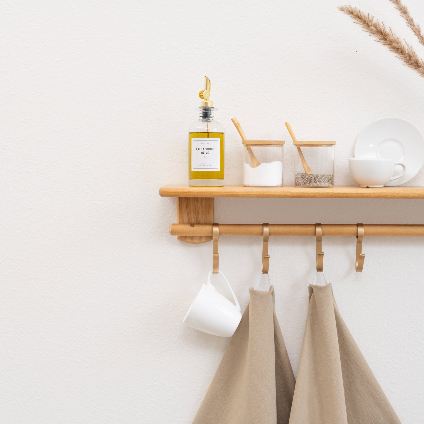 Wooden shelf with kitchen items and aprons hanging on hooks against a white wall.