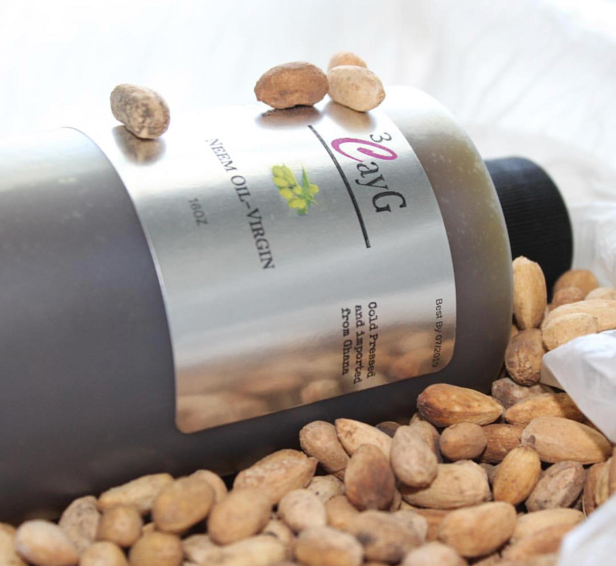 Bottle of 3CAYG neem oil surrounded by nuts on a white background