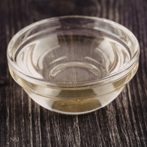 Clear glass bowl with squalane oil on a wooden surface
