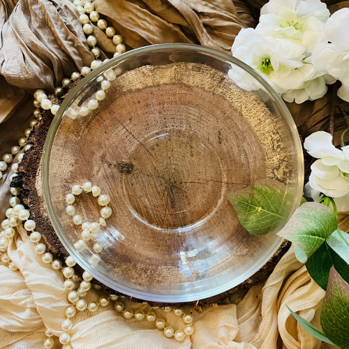 Flat lay of preservatives in skincare in a clear glass bowl on a wood slab with neutral background