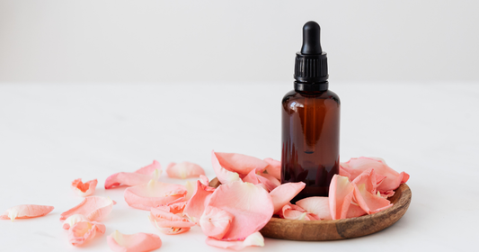 Restorative botanical facial oil in amber bottle on wood plaque with pink rose petals on a neutral background
