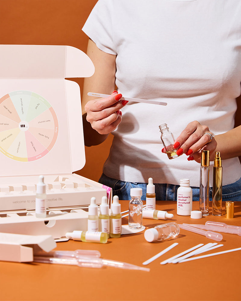 Person holding a dropper and a bottle with various skincare products on an orange surface.