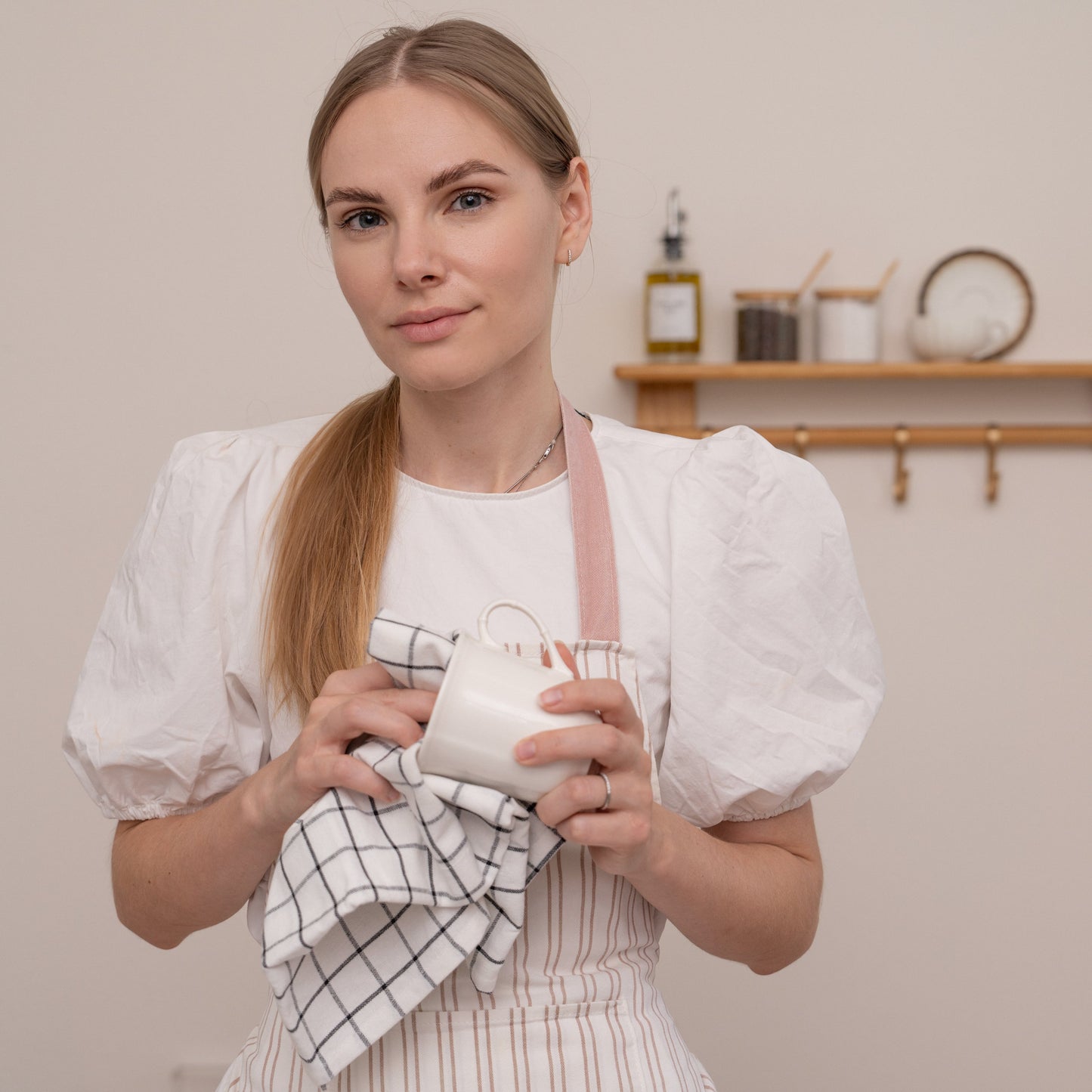 Woman holding a ceramic mug and a towel in a kitchen setting