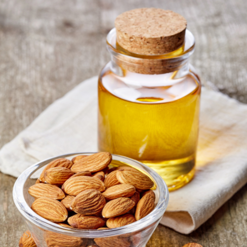 Bottle of almond oil on a linen napkin with a clear glass bowl of almond on a neutral background
