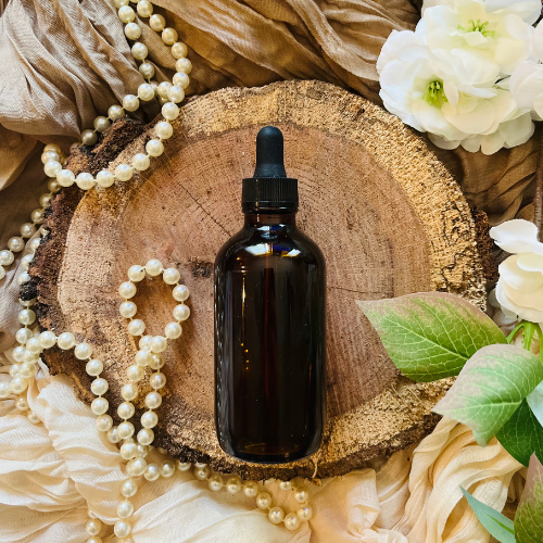 Dark glass bottle with dropper on a wooden surface with pearls and flowers
