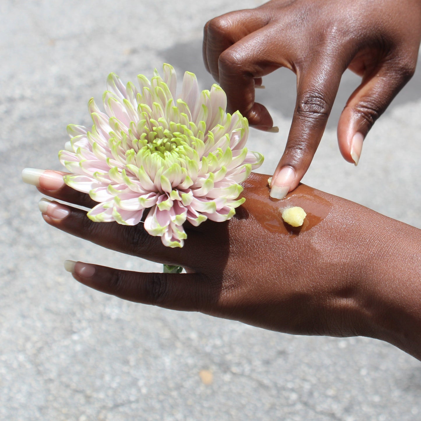 Hand applying a product to another hand with a flower nearby
