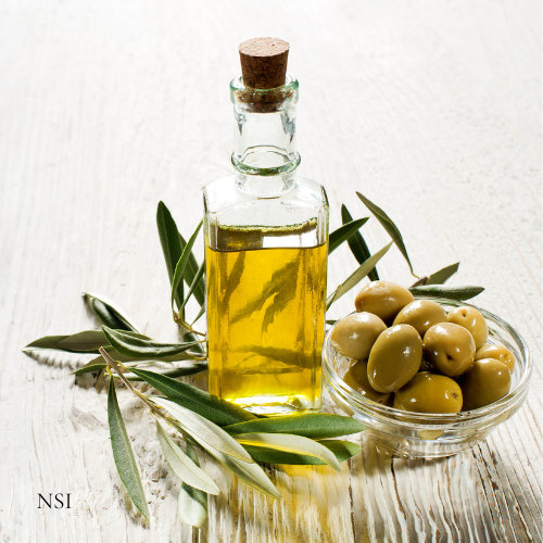 Bottle of Extra Virgin Organic Olive Oil on a neutral background with a clear bowl of olives