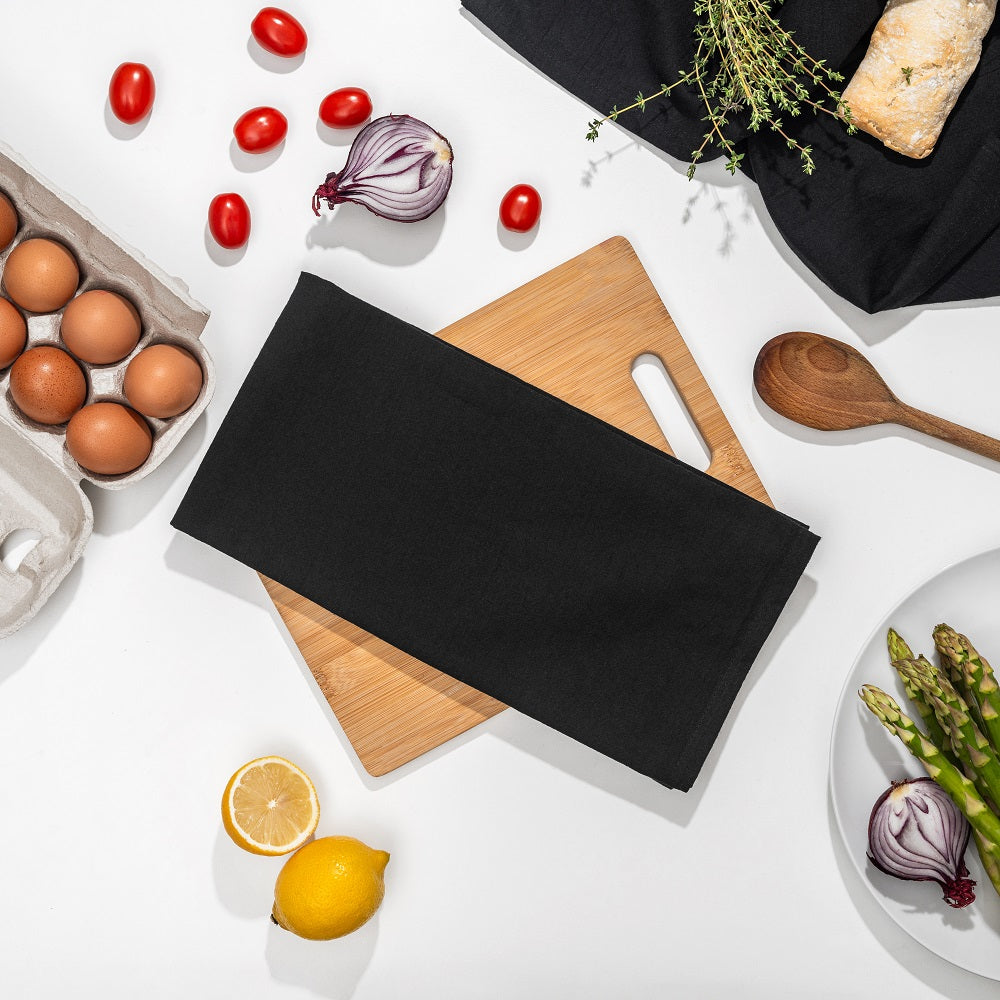 Black kitchen towel draped over a wooden cutting board with various kitchen items on a white surface.