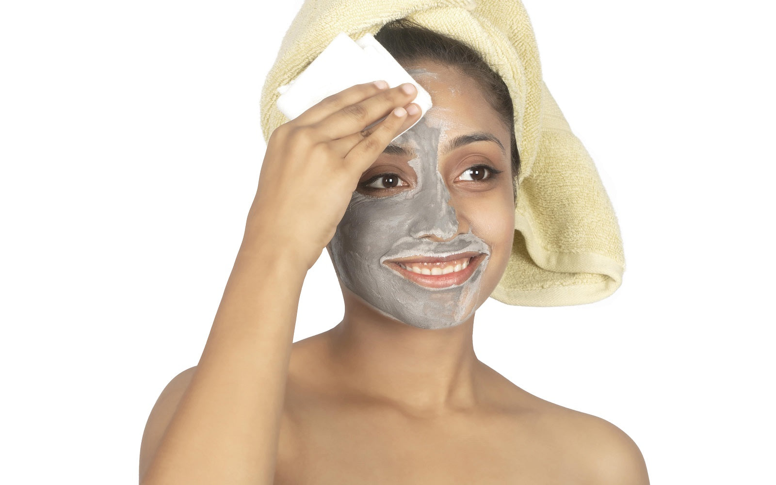Woman applying a gray facial mask with a towel on her head against a white background