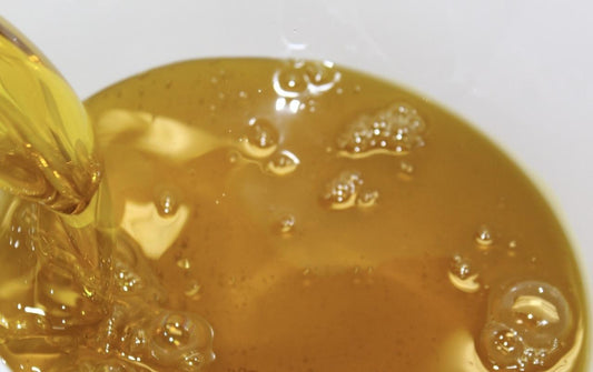 Close-up of hibiscus seed oil being poured into a bowl with a white background