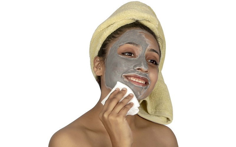 Woman applying a gray facial mask with a towel on her head against a white background