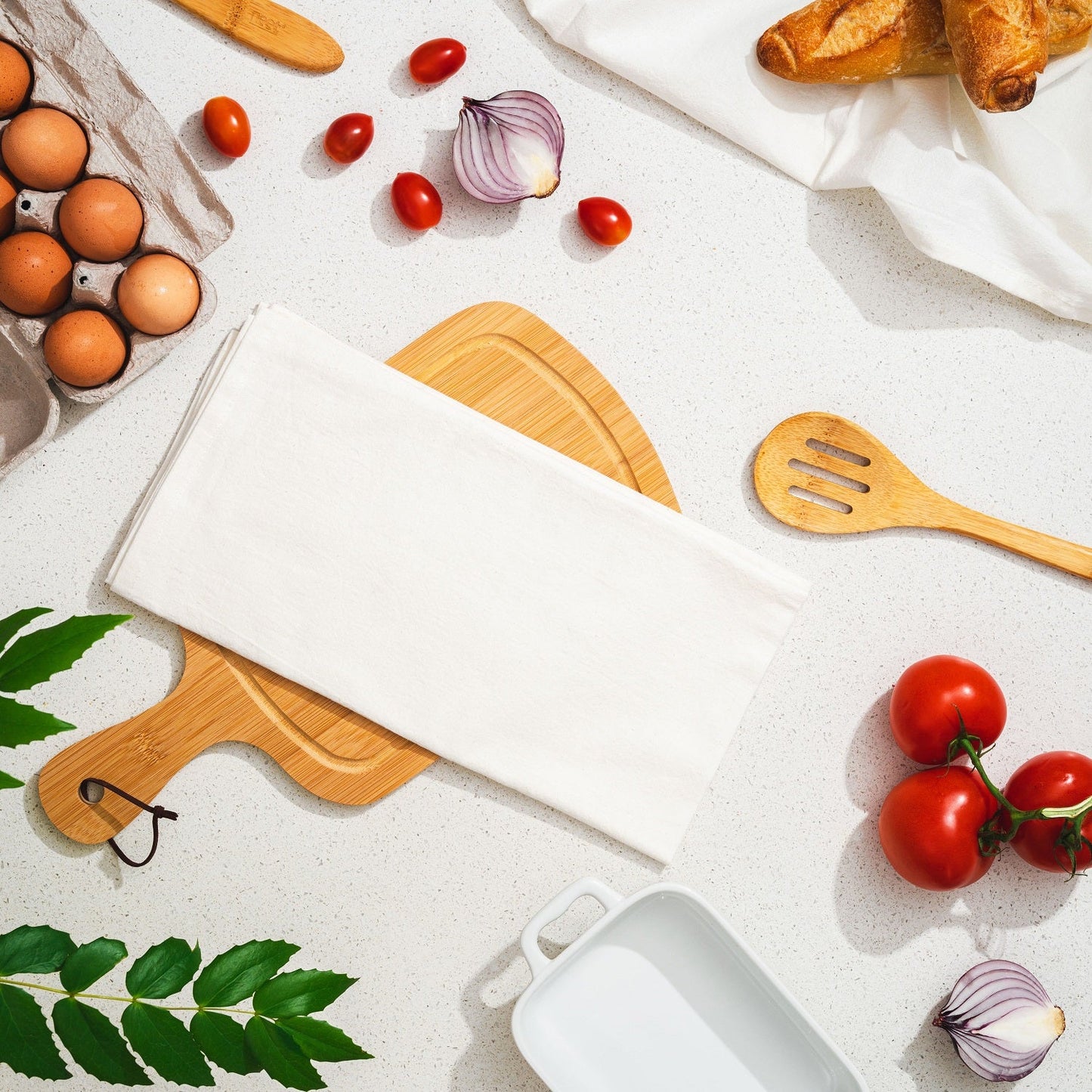 Kitchen counter with cutting board, eggs, tomatoes, and wooden utensils on a light background