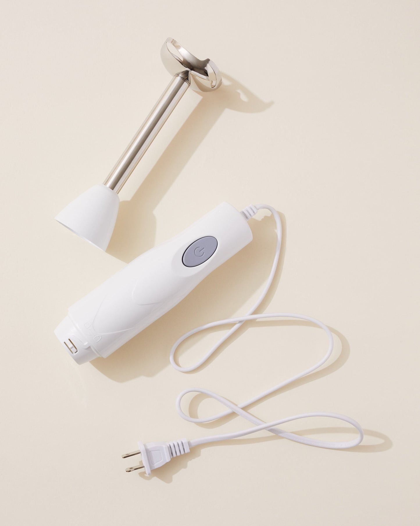 White handheld blending device with a cord on a beige background
