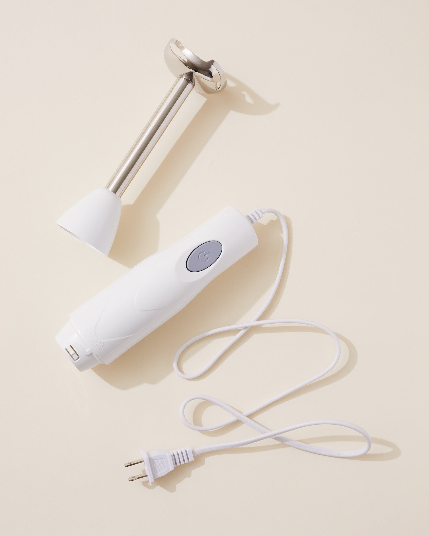 White handheld blending device with a cord on a beige background