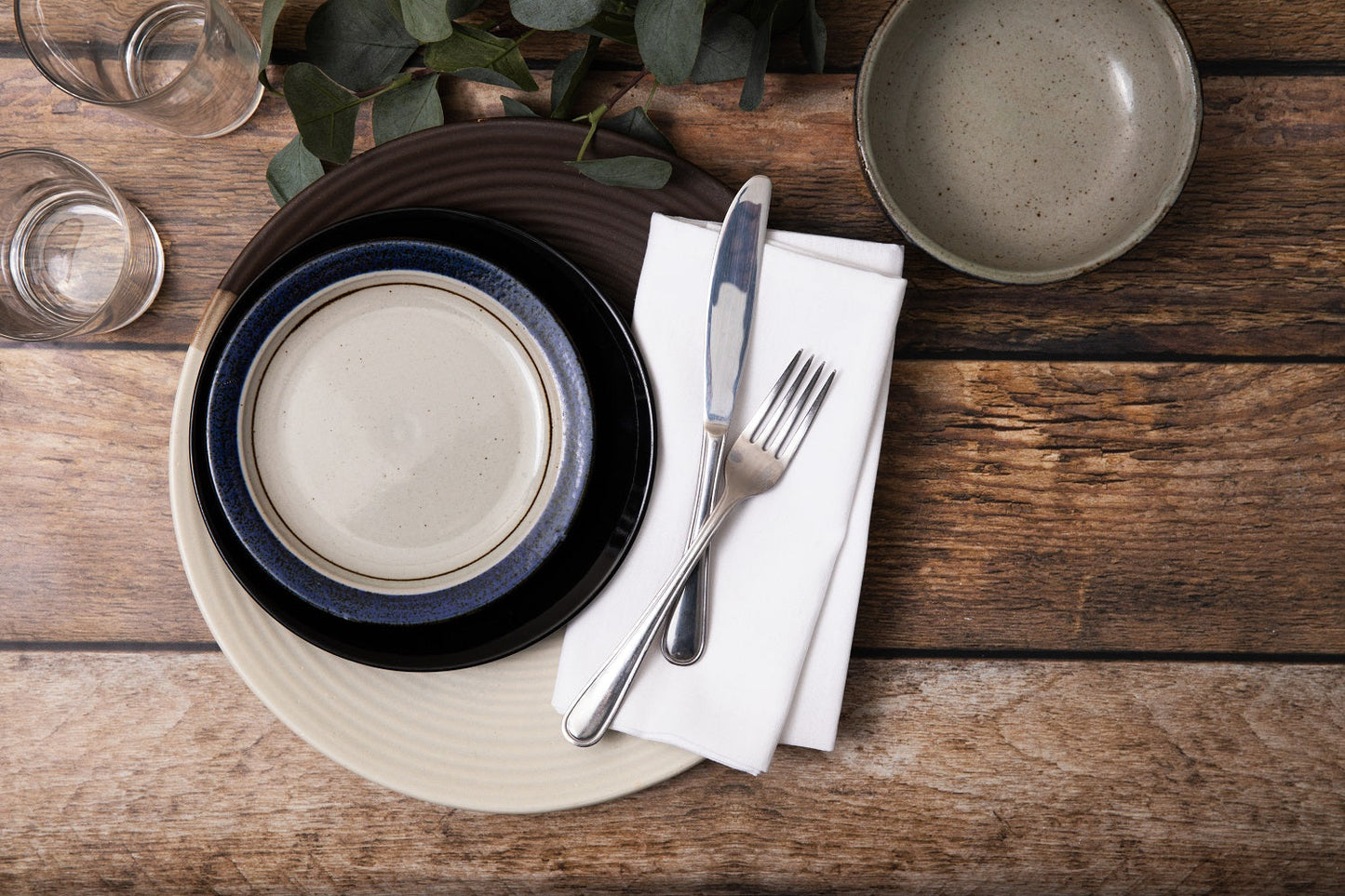 Dining table setting with ceramic plates, cutlery, and glasses on a wooden surface.
